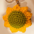 Crocheted sunflower keychain with a gold ring on a beige background