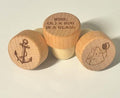 Three wooden wine bottle stoppers with engraved designs and text on a light background