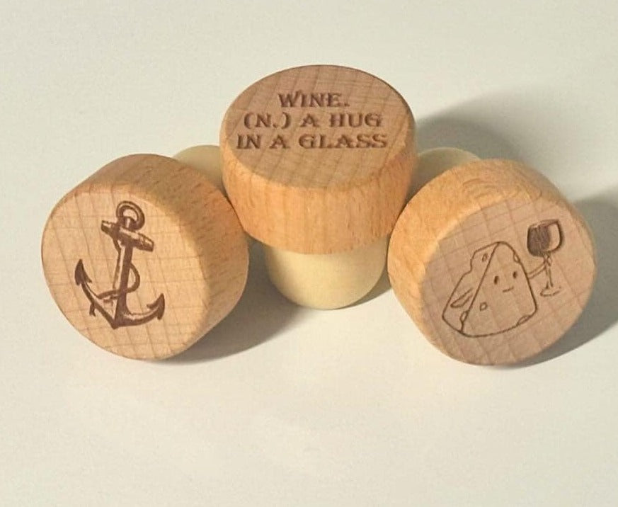 Three wooden wine bottle stoppers with engraved designs and text on a light background