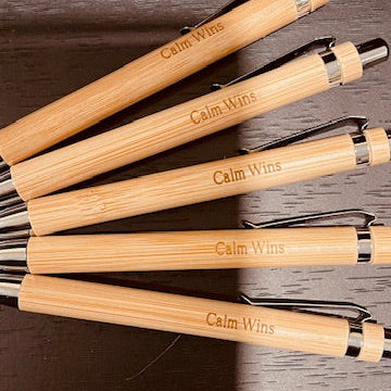 Set of wooden pens with 'Calm Wins' engraving on a dark surface