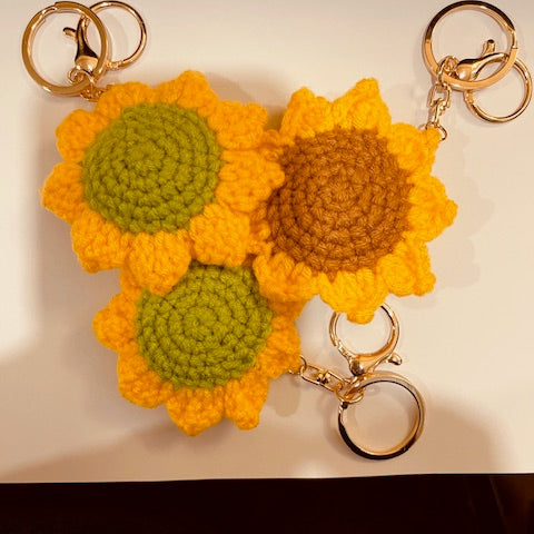 Two sunflower-shaped keychains with gold rings on a beige background